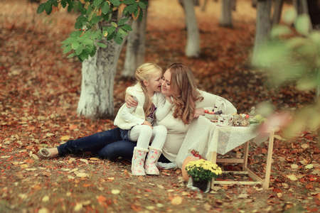 autumn warm day in the woods on a picnic table with fruits and dishes sitting mother with her daughterの写真素材