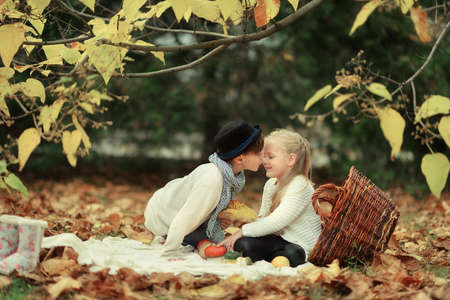 golden autumn forest picnic, boy in a hat with a cute little girl in a big basketの写真素材