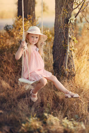 in the park near the big trees ride on a swing Pretty girl with long hair and a hatの写真素材