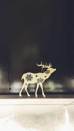 on the window sill at the window with frost on the glass is a wooden deer with snowflakesの写真素材