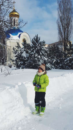 winter park trees and bushes in a fluffy snow on the background of the church and the boy with red cheeks from the coldの写真素材
