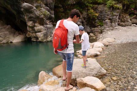 father with a red backpack trip with his son on a mountain riverの写真素材