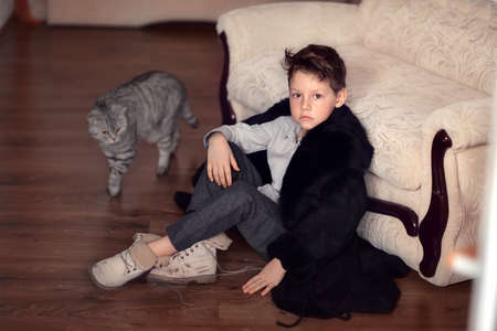 sitting on the floor of a little boy with a stylish haircut in a fur coat and bootsの写真素材