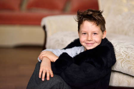 portrait of a little boy sitting with a stylish haircut in a black fur coatの写真素材