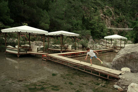 mountains in the background on the river are home and the wooden bridge it walks a boy in a capの写真素材