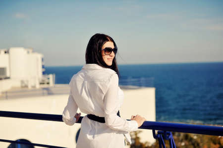 against the backdrop of the azure sea near the fence stands a woman with long black hair wearing...