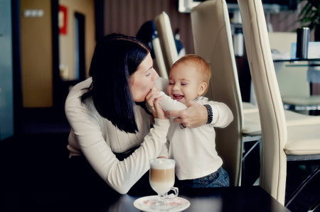 happy mother with a young son sitting at the table and on the table with a glass of latteの写真素材