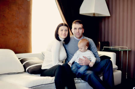 room on a white couch sits a young family with little sonの写真素材