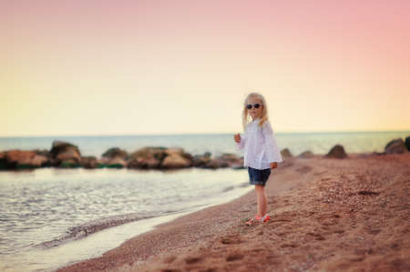 against the sky blonde little girl in sunglasses walking on the beachの写真素材