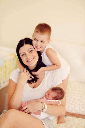 mother with long black hair with two young sons on the bedの写真素材