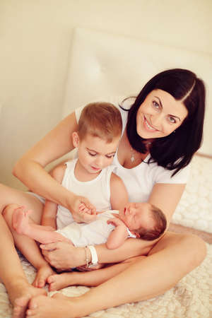 mother with long black hair with two young sons on the bedの写真素材