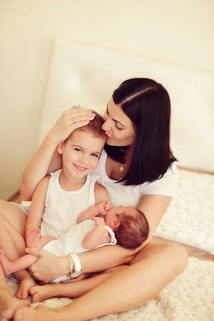 mother with long black hair with two young sons on the bedの写真素材