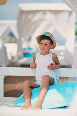 against the backdrop of the sea and the deck sitting on a blue pillow boy in a hatの写真素材