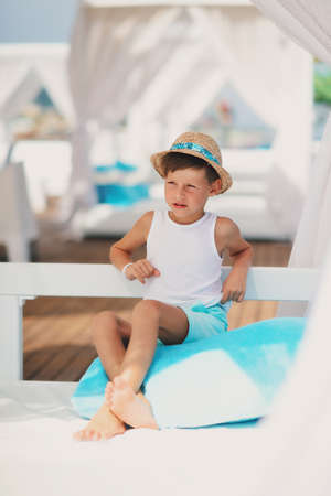 against the backdrop of the sea and the deck sitting on a blue pillow boy in a hatの写真素材