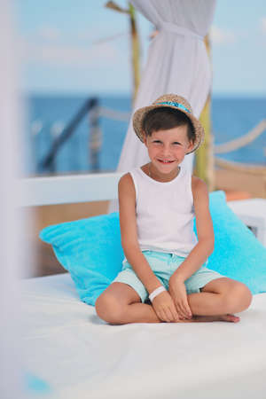 against the backdrop of the sea and the deck sitting on a blue pillow boy in a hatの写真素材