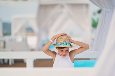 against the backdrop of the sea and the deck sitting on a blue pillow boy in a hatの写真素材