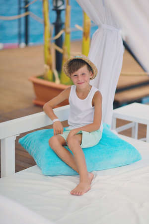 against the backdrop of the sea and the deck sitting on a blue pillow boy in a hatの写真素材