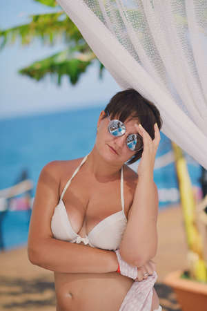 under a canopy near the sea woman in swimsuit and sunglassesの写真素材
