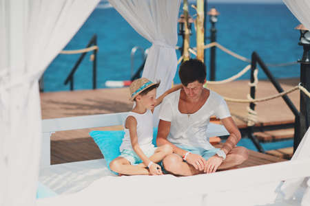on the background of the sea under a canopy dad with a young son in a hat carrying on a conversationの写真素材