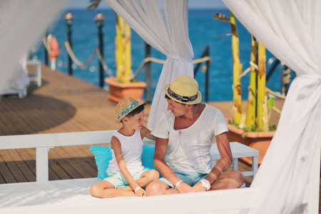 on the background of the sea under a canopy dad with a young son in a hat carrying on a conversationの写真素材