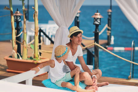 on the background of the sea under a canopy dad with a young son in a hat carrying on a conversationの写真素材
