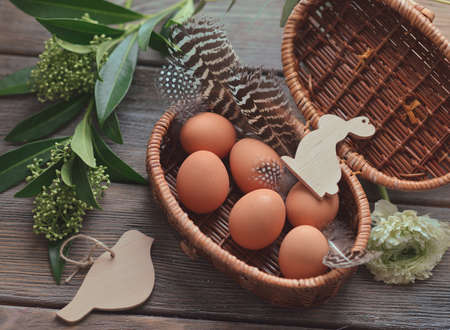 on a wooden table wicker basket with eggs feathers and flowers