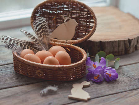 on a wooden table wicker basket with eggs feathers and flowersの写真素材