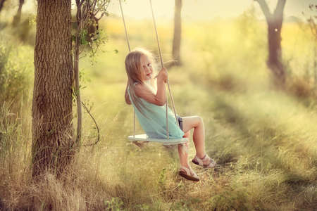 in the park near the big trees ride on a swing Pretty girl with long hairの写真素材