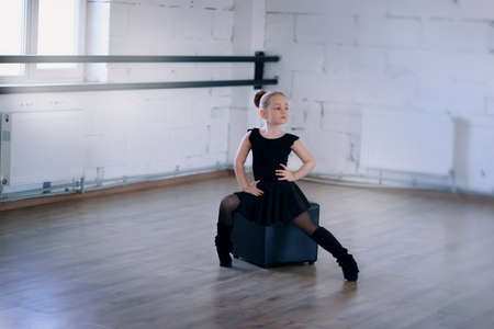 little ballerina in a black dress in pantyhose sitting on a black square in the hallの写真素材