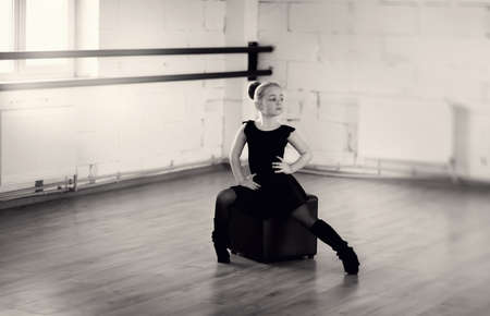 little ballerina in a black dress in pantyhose sitting on a black square in the hallの写真素材