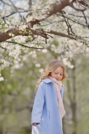 spring sunny day blond girl in blue coat in the lush gardenの写真素材