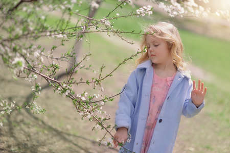 spring sunny day blond girl in blue coat in the lush gardenの写真素材