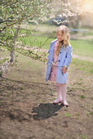 spring sunny day blond girl in blue coat in the lush gardenの写真素材