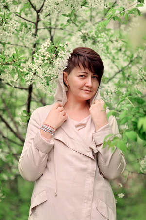 Woman with stylish hairstyle and light raincoat in the lush gardenの写真素材