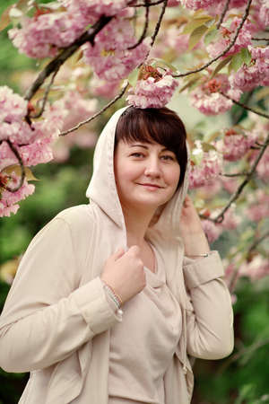 Woman with stylish hairstyle and light raincoat in the lush garden near the cherryの写真素材