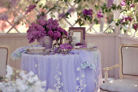 white gazebo a table with dishes and a dessert and a vase with a bouquet of lilacsの写真素材