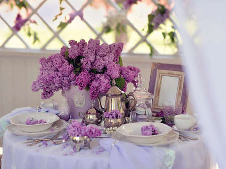 white gazebo a table with dishes and a dessert and a vase with a bouquet of lilacsの写真素材
