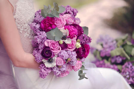 bride in a white dress holding a beautiful bouquet of lilacs and rosesの写真素材