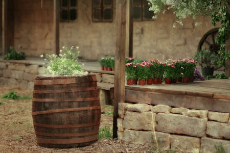 in the courtyard of a stone house on the porch with pots of flowers and a big barrel with flowersの写真素材