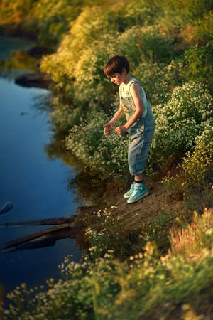 Summer sunset at the river cute boy in jeans looking at the waterの写真素材