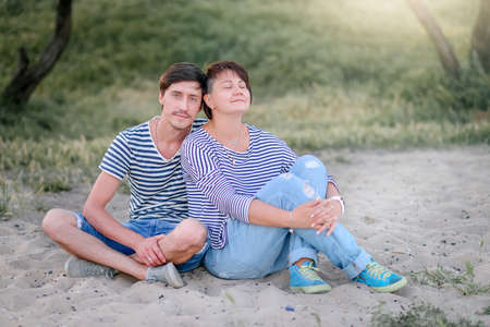 on the background of trees and sunset young couple sitting on the sand vestsの写真素材