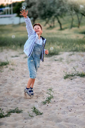 cheerful and happy little boy in jeans catches soap bubbles in the parkの写真素材