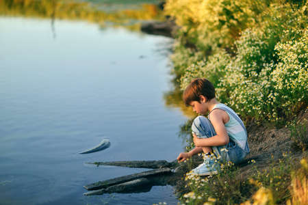 summer evening, a little boy in jeans playing in the grass by the riverの写真素材