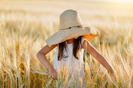 little girl in a straw hat and with long hair on a field of wheatの写真素材