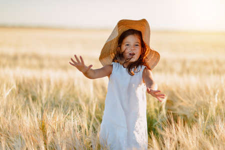 little girl in a straw hat and with long hair on a field of wheatの写真素材