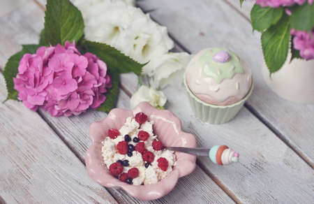 on a wooden board flower arrangement of tender buds and a plate with a dessert of berriesの写真素材
