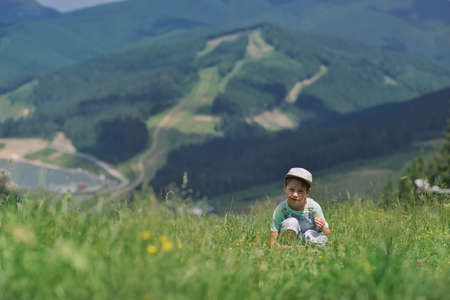 cute little boy in denim overalls and a cap sitting on logs mountains in the backgroundの写真素材
