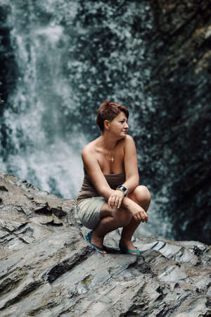 Against the of a waterfall on a large rock sitting womanの写真素材