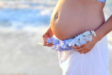 sunny day on the background of the sea pregnant woman's belly with a wreath of flowers in their handsの写真素材