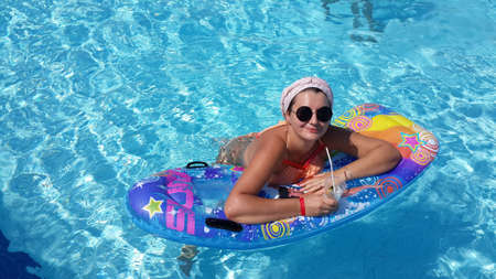 in the azure pool floating on a mattress woman in sunglasses with a cocktail in handの写真素材
